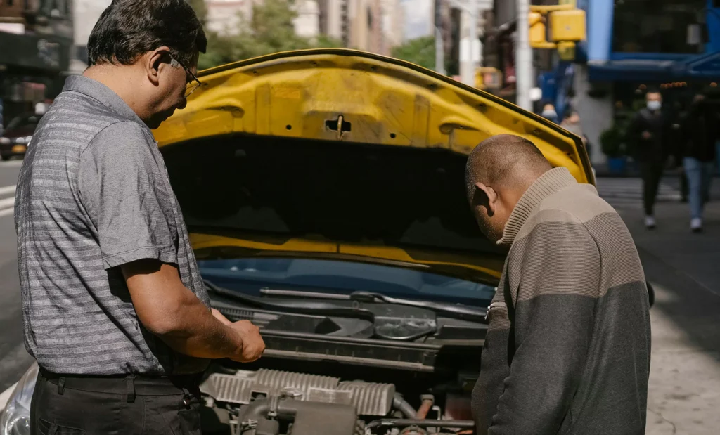 Dois homens olhando motor do carro em uma via pública